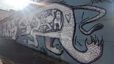 A large street mural shows a stylized face and sweeping line art on a wall.