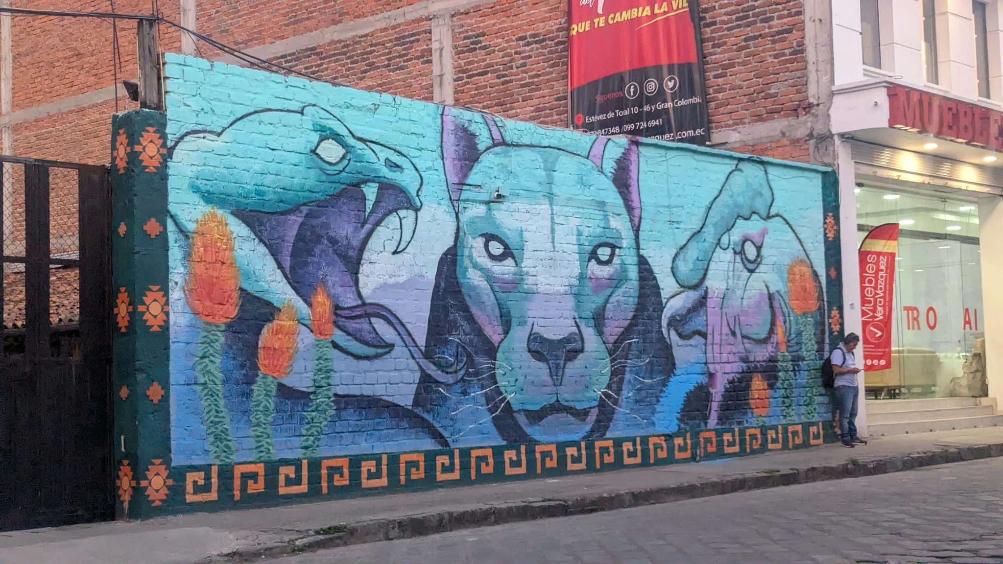 A blue mural with stylized figures covers a street wall.