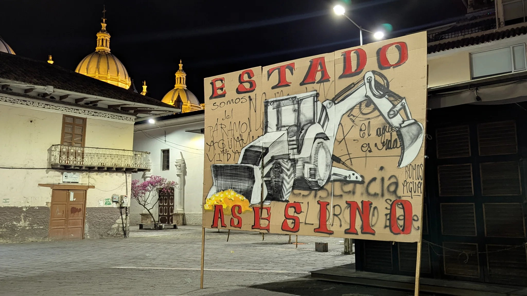 A colorful night mural and church tower are lit in an urban plaza.