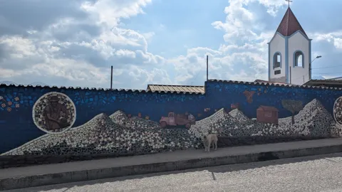A mural with a church and decorative figures stretches along a wall.