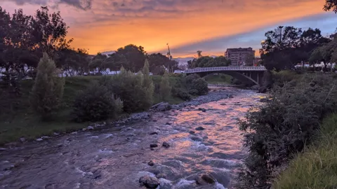 A rocky river reflects orange sunset light with trees along the banks.