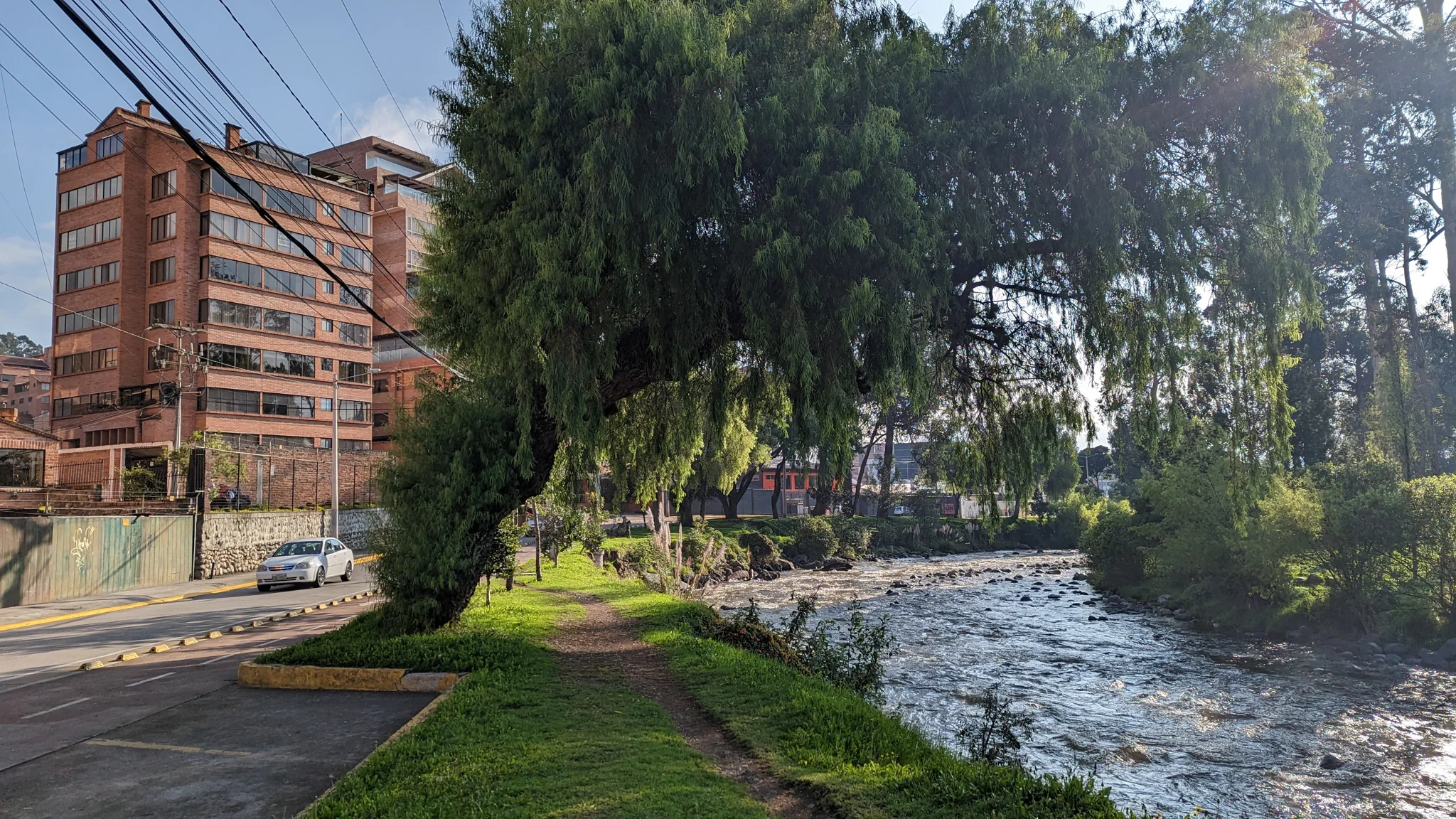 A red brick building stands near a riverfront lined with trees.