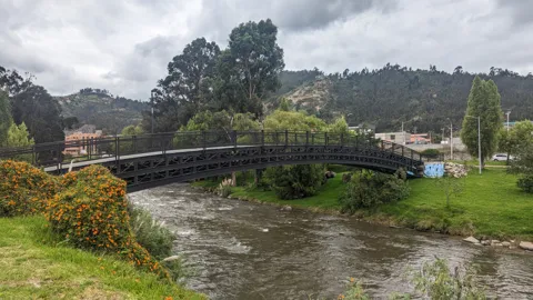 River running below a pedestrian bridge and riverside buildings.
