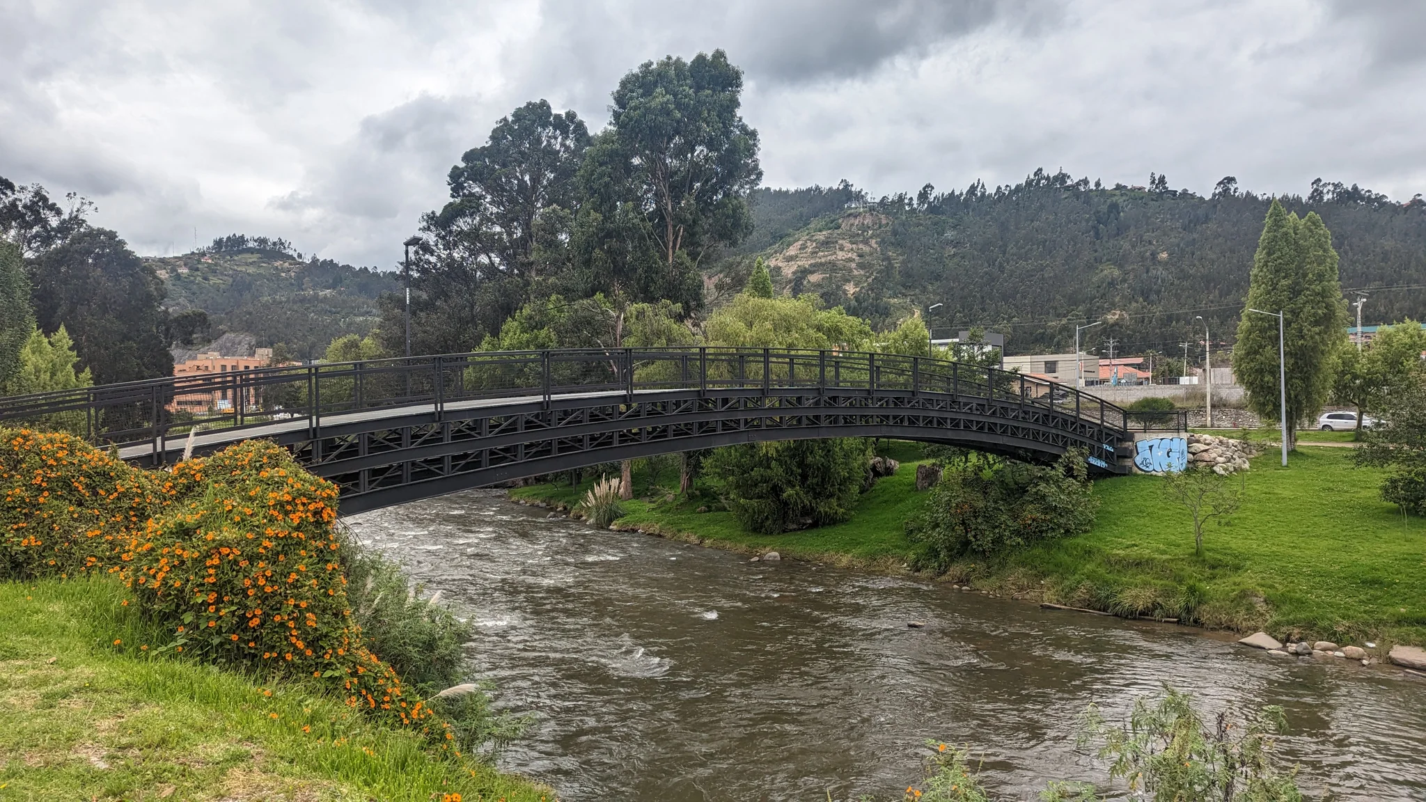 River running below a pedestrian bridge and riverside buildings.
