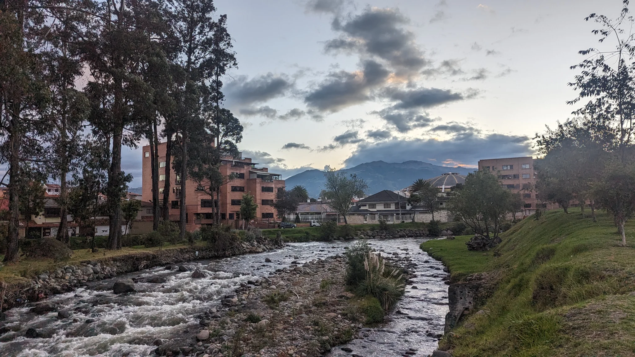 River bend through an urban park with trees and mountains beyond.