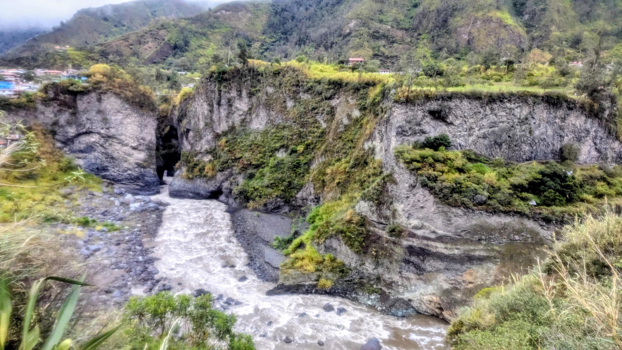 Water cascades over layered rocks through a green highland valley.