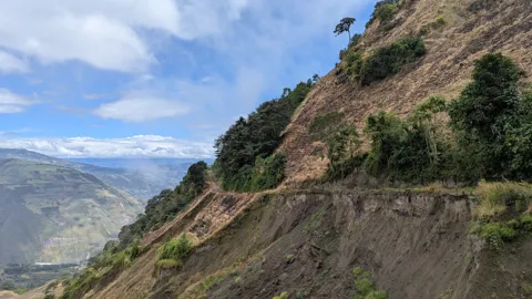 A rocky hillside drops toward a valley with mountains in the distance.