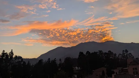 Dramatic sunset clouds glowing over mountains and trees.