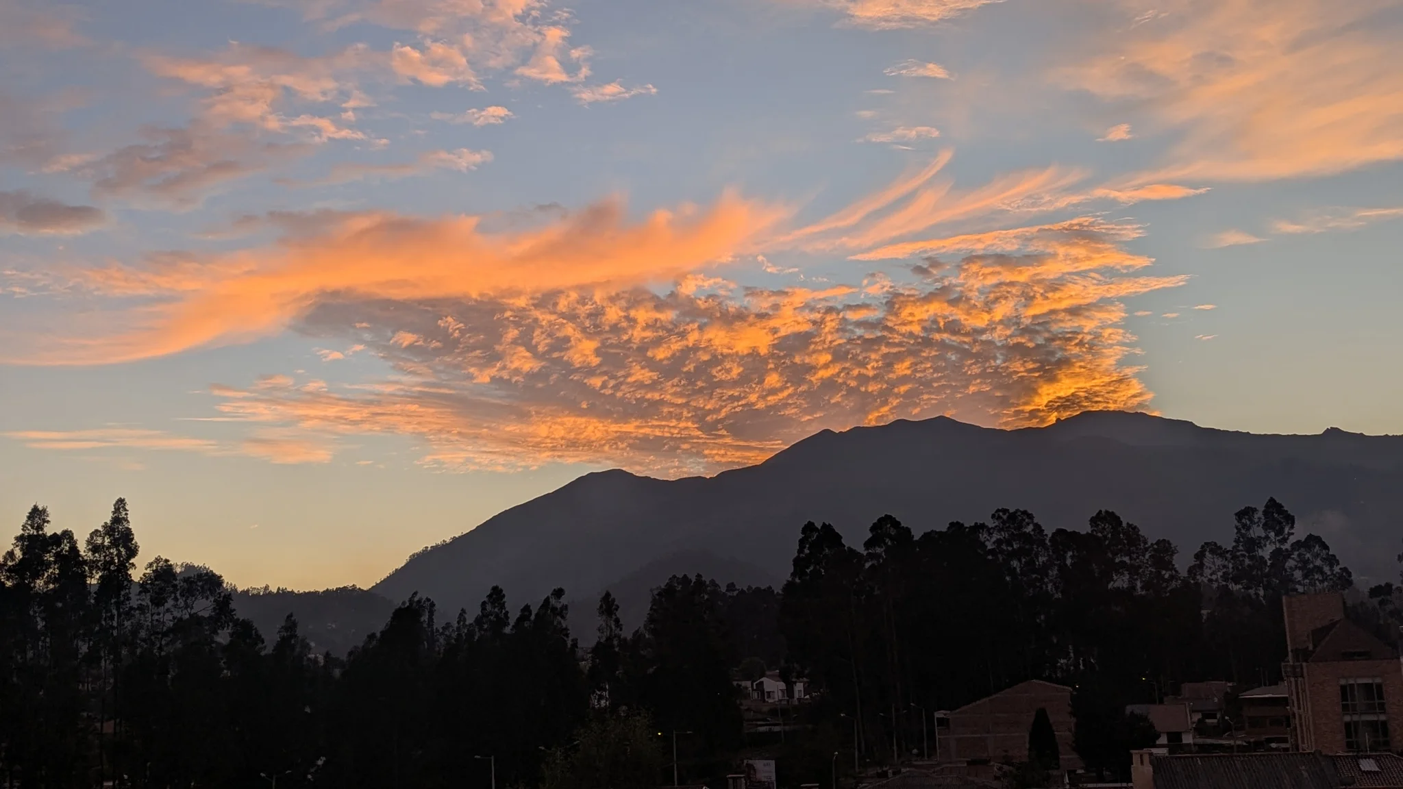 Dramatic sunset clouds glowing over mountains and trees.