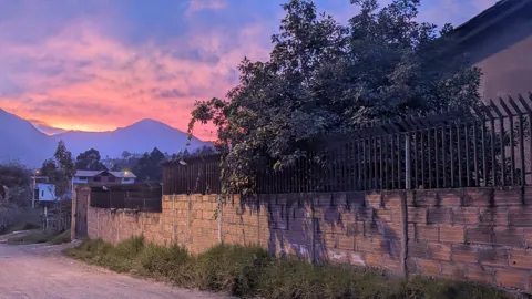 Purple and pink sunset clouds glow above dark trees and mountain silhouettes.
