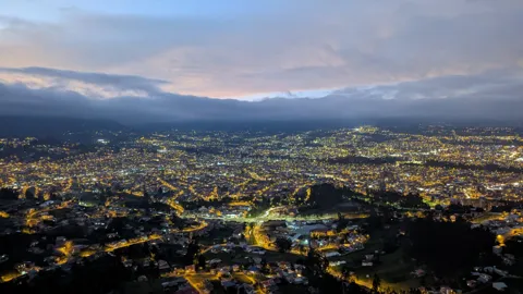 City lights glow below layered clouds after sunset.