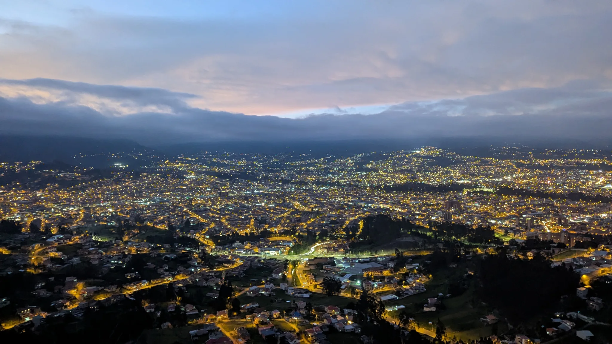 City lights glow below layered clouds after sunset.
