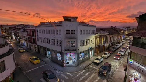 Orange sunset light fills the sky above a city street and corner building.