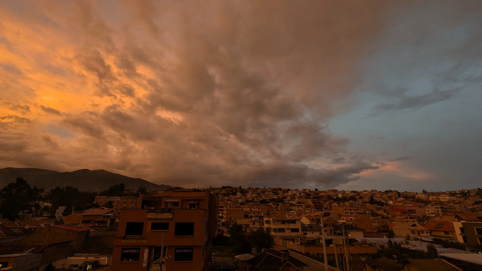 Orange storm clouds glowing over hills and city rooftops.