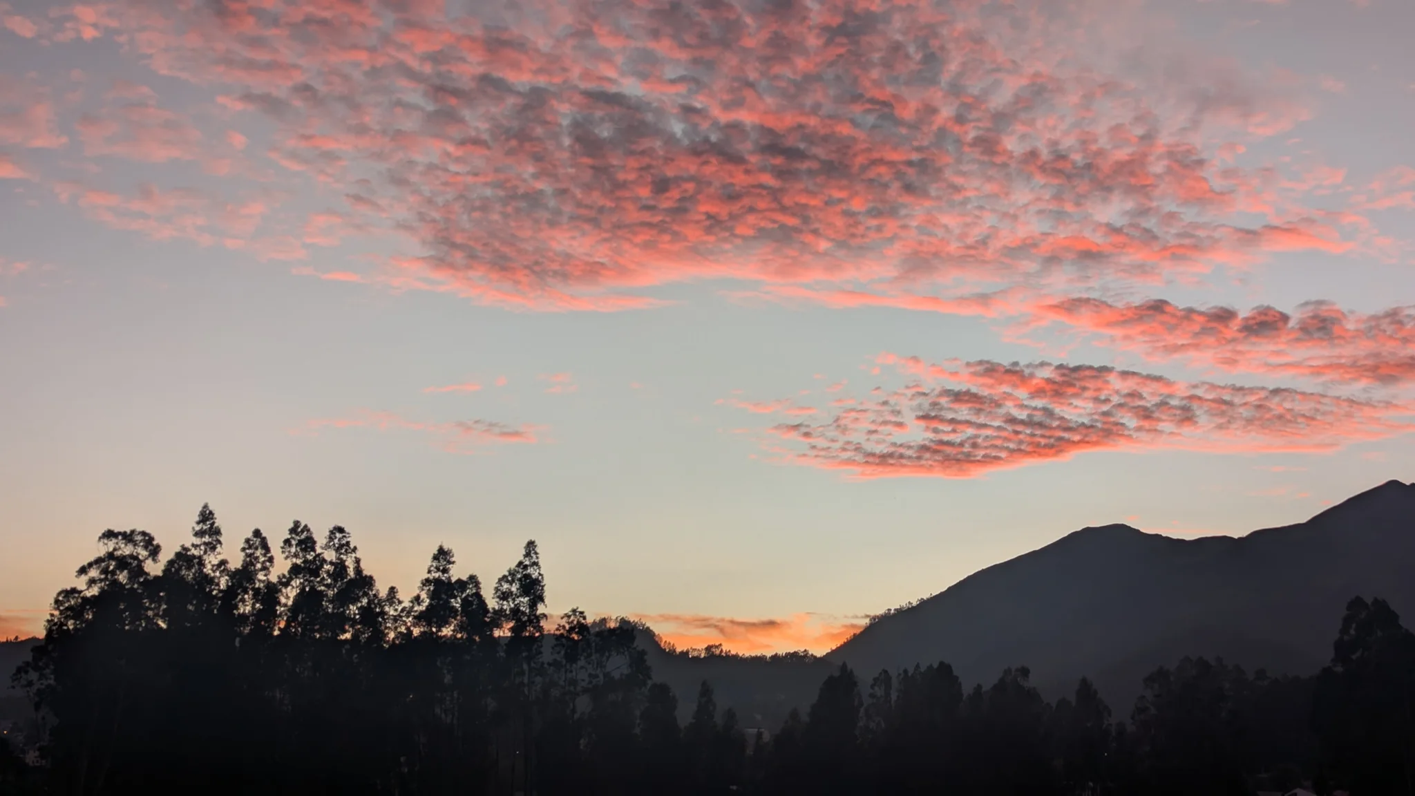 Soft pink sunset clouds above the hills and trees.