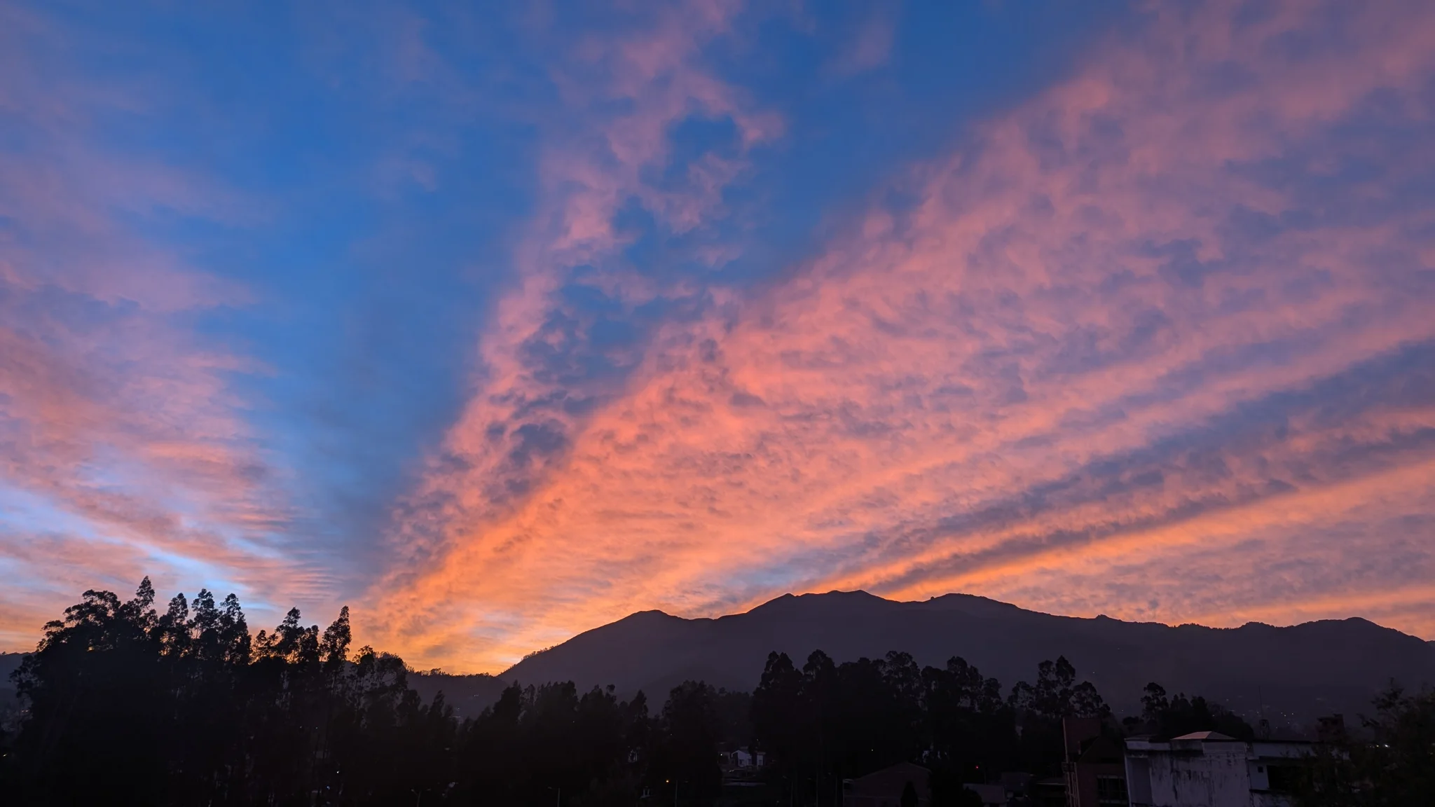 Bright streaks of pink sunset cloud above dark mountain silhouettes.