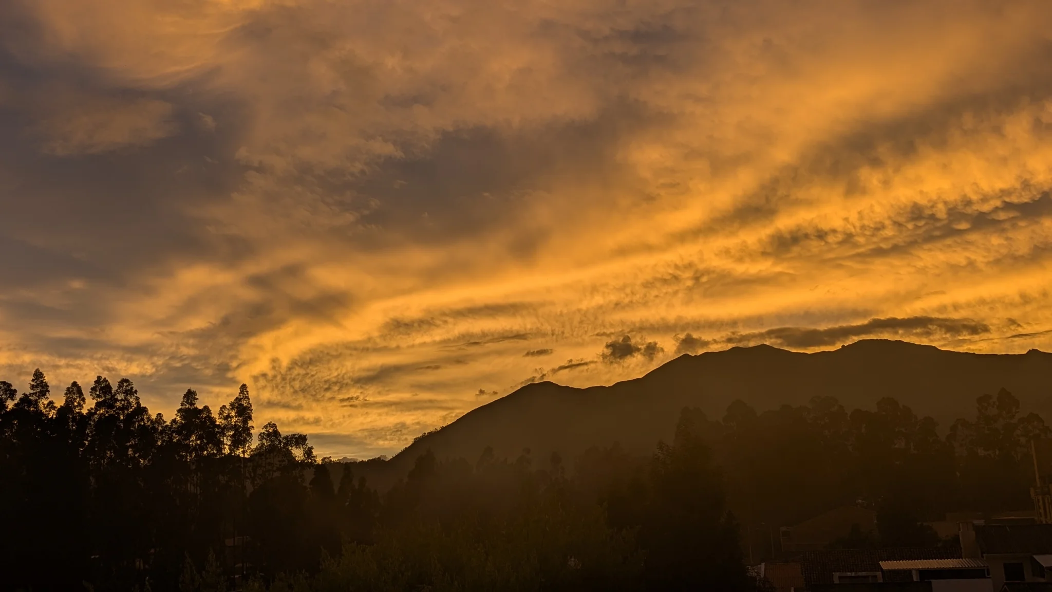 Dramatic orange sunset clouds over dark mountain silhouettes.