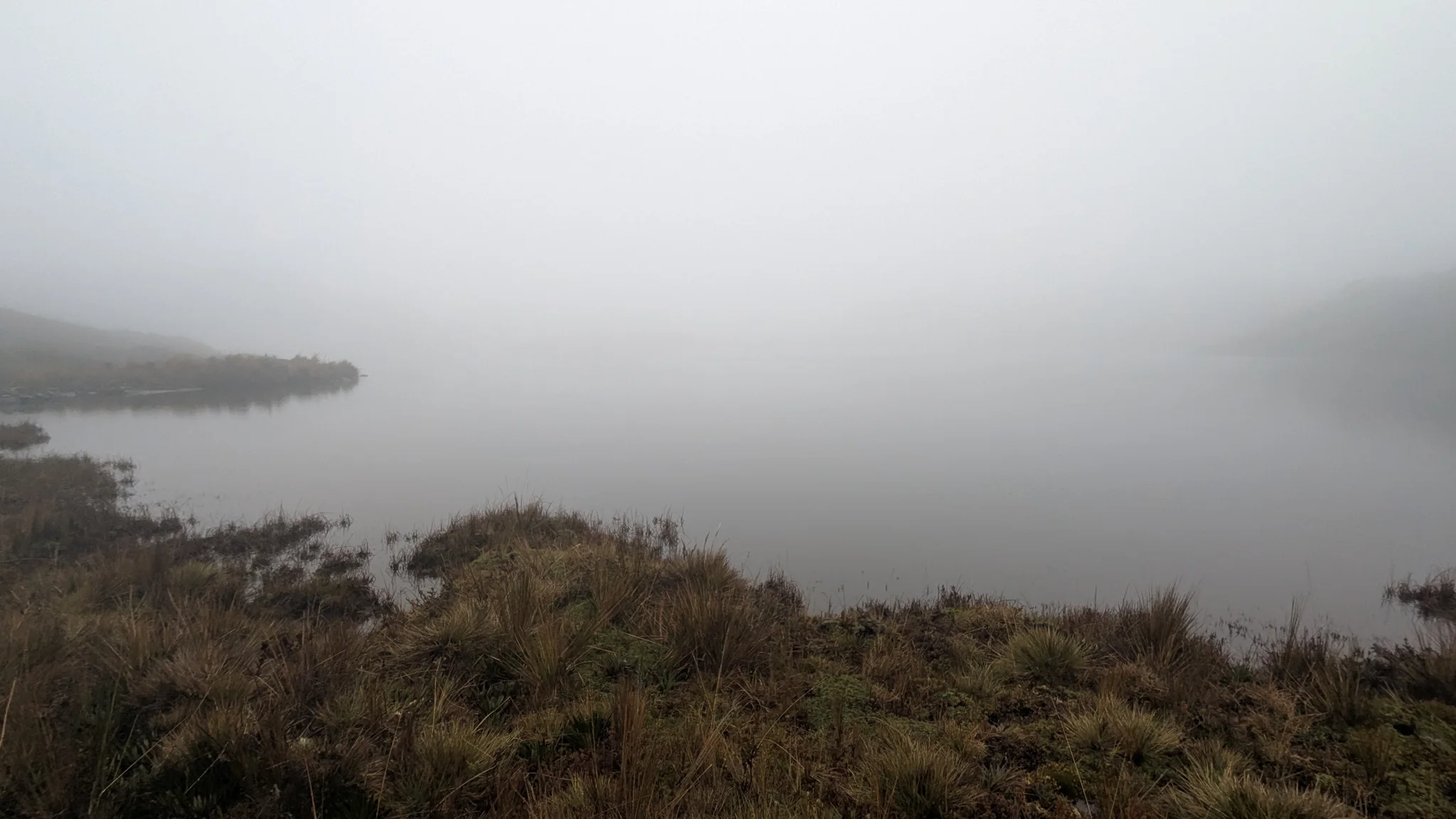A dark headland fades into low fog above still water during the Osohuayco outing. The lake is not securely named.