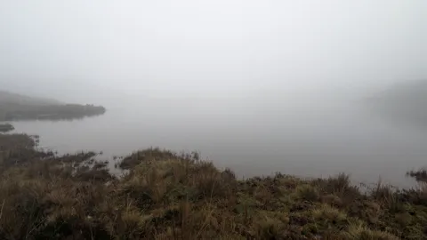 A dark headland fades into low fog above still water during the Osohuayco outing. The lake is not securely named.
