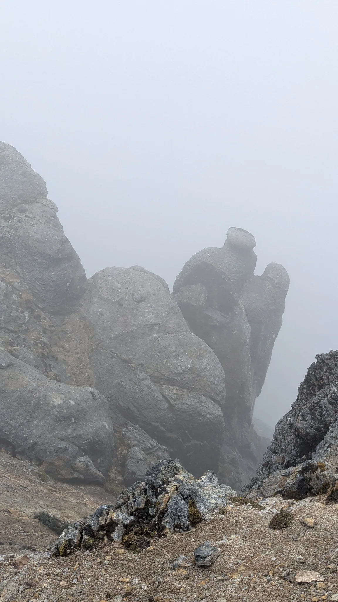 A narrow rock pinnacle rises beside fractured slabs and vanishes into the mist.