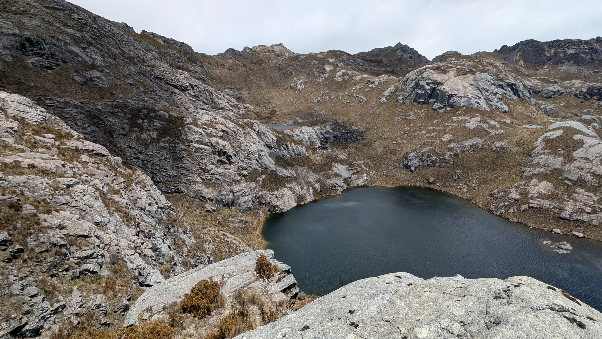 A dark, unnamed tarn fills a steep rocky hollow below a broad highland overlook.