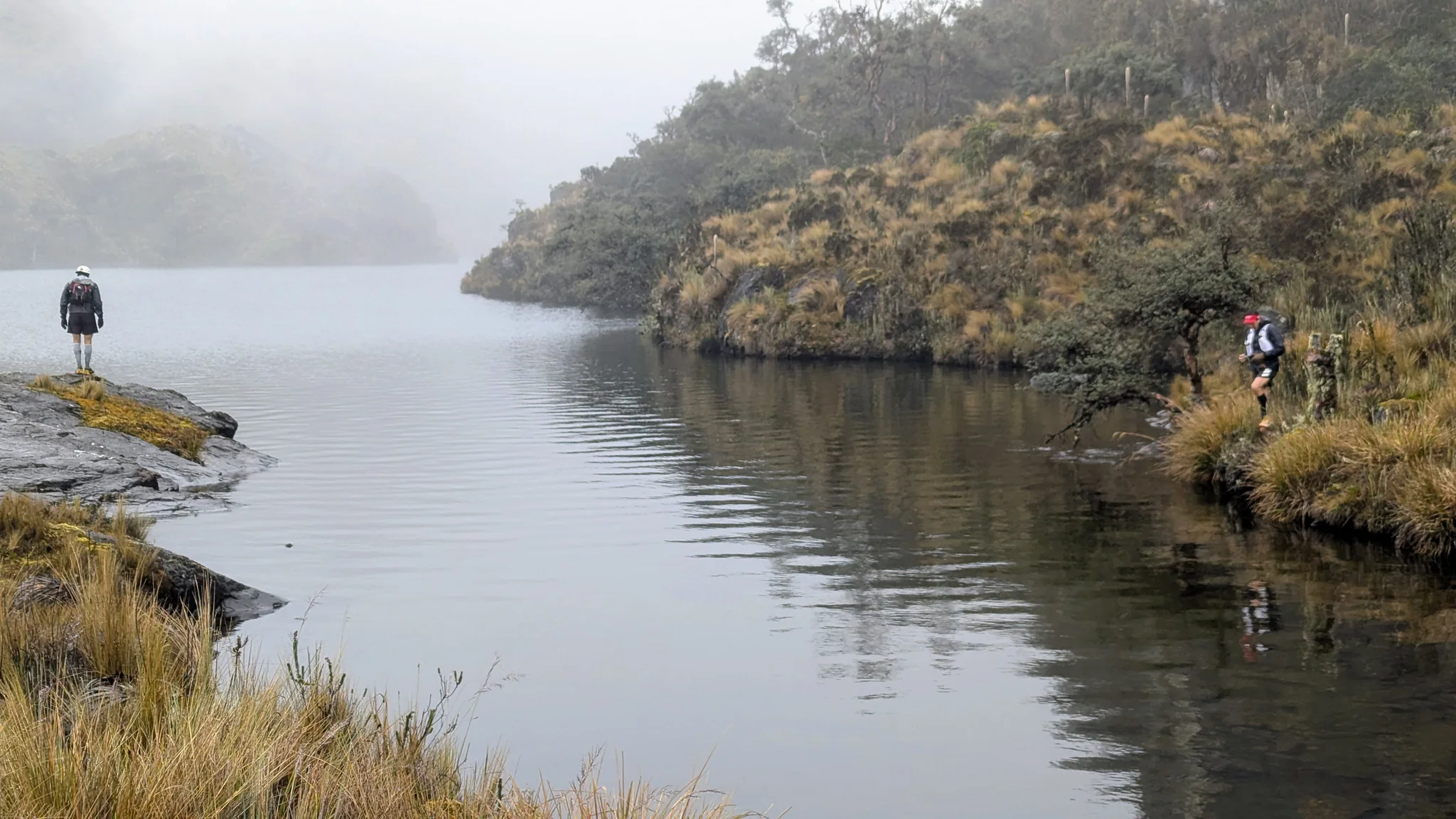 Hikers on opposite sides of a lake inlet. The water body is not securely named.