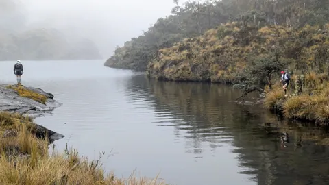 Hikers on opposite sides of a lake inlet. The water body is not securely named.