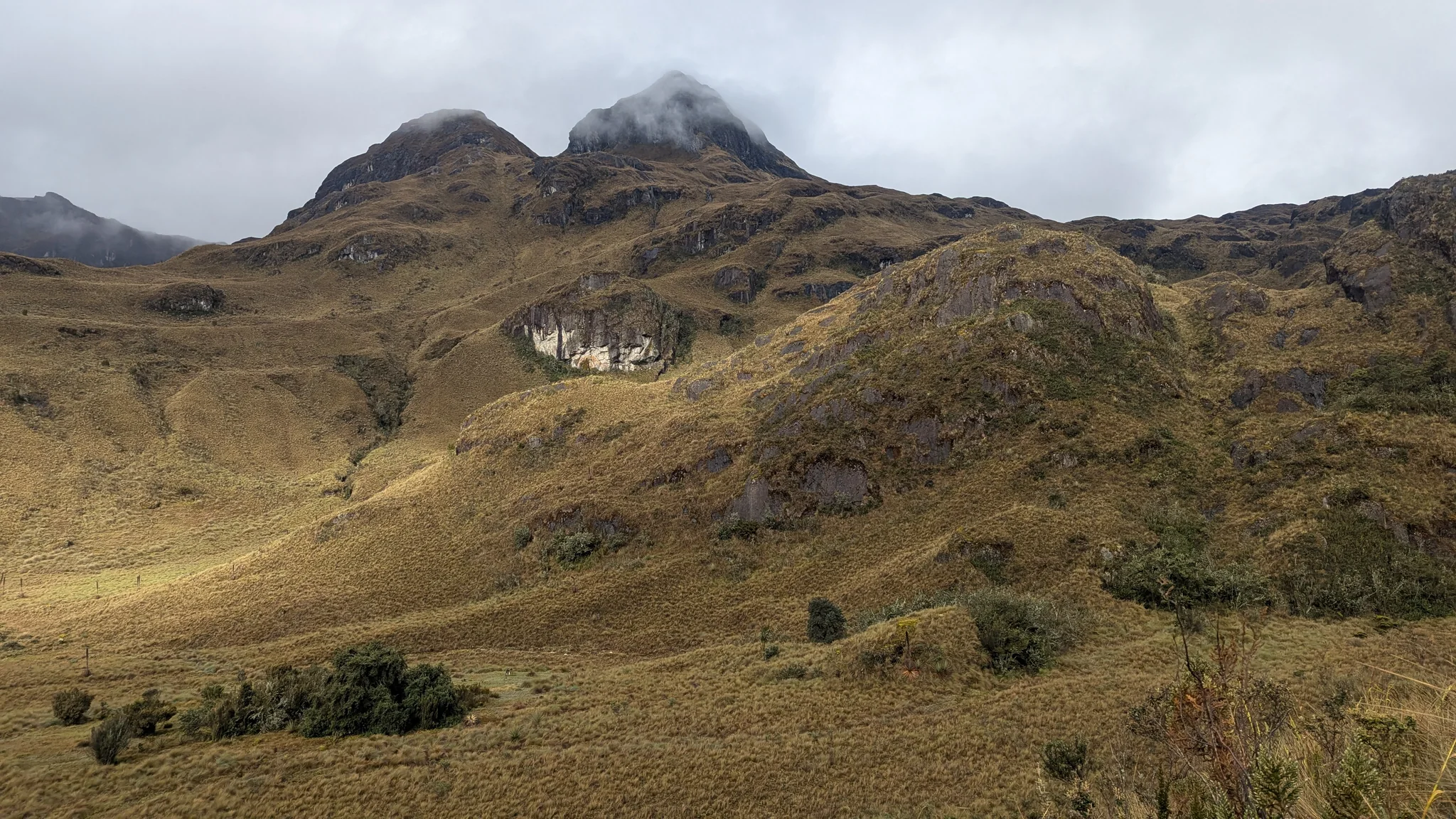 Low cloud curls around two rocky summits above open páramo slopes. The peaks are left unnamed.