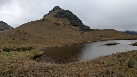 An unnamed dark lake curves below a pointed grassy hill during the Cajas crossing.