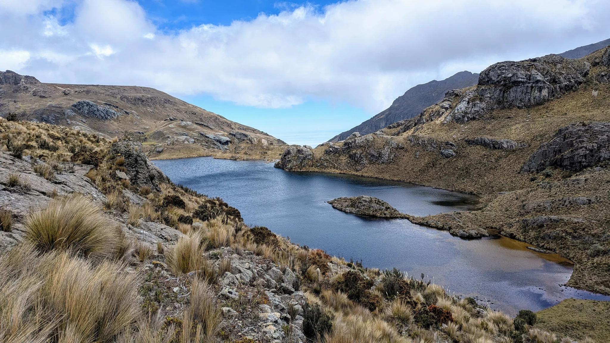 Estrellascocha de Quitahuaycu curves around a rocky peninsula below open highland slopes.