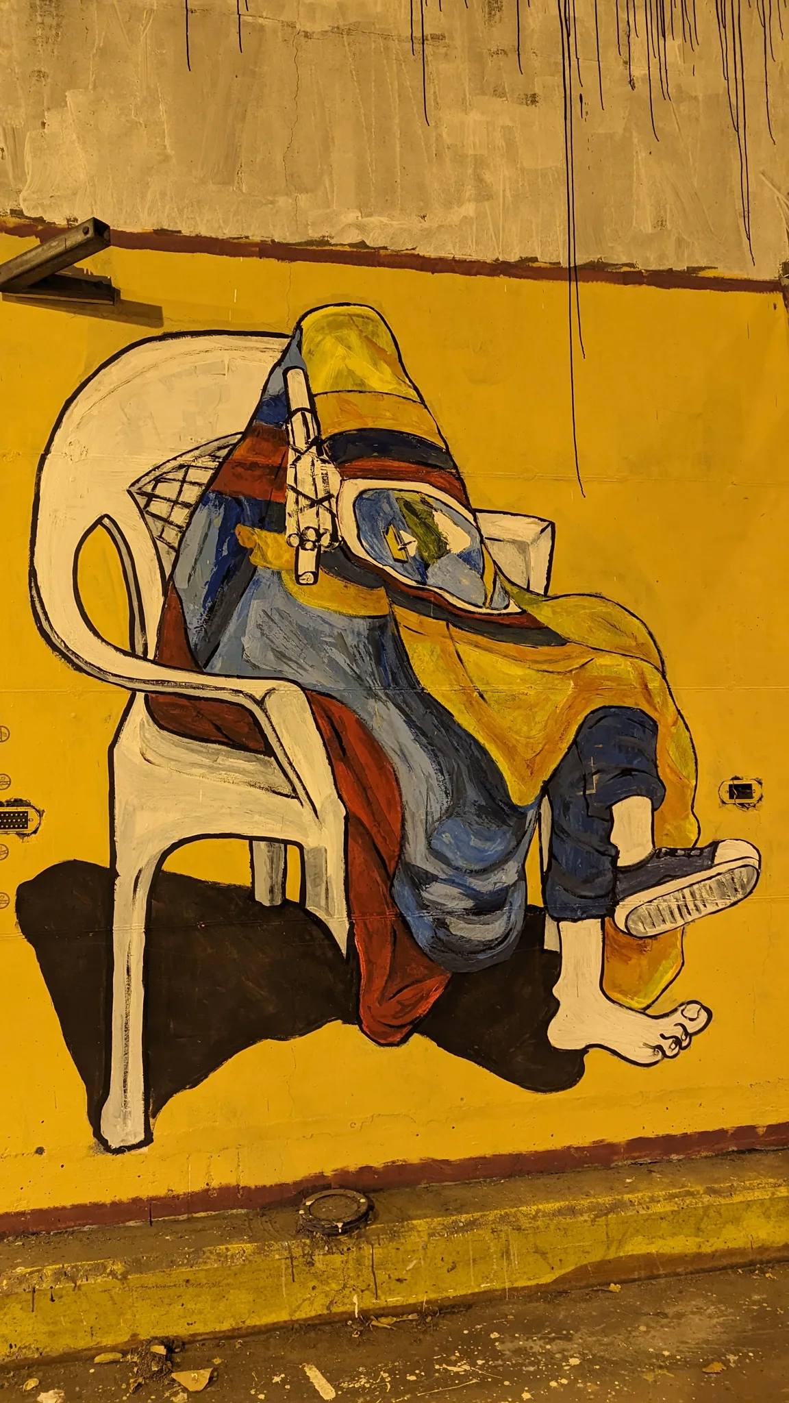 A seated figure on a yellow wall